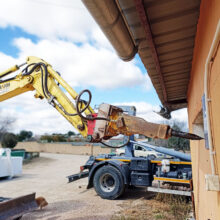 Brazo de excavadora, con accesorio de pico - demolición, apoyado sobre el muro de una casa cuyo derribo va a comenzar.